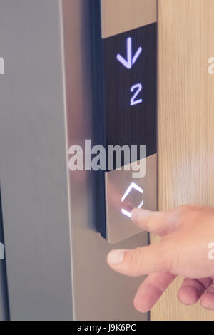 Male forefinger pushing down arrow elevator button. Digital display showing second floor. Modern buildings and technology concepts Stock Photo