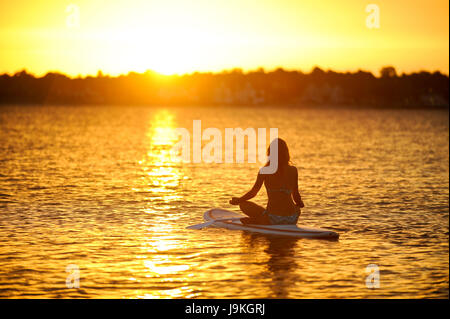 young woman doing yoga on a surfboard Stock Photo