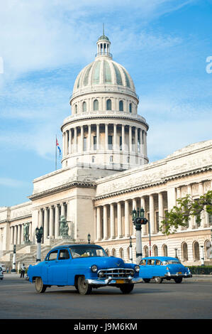 Brightly colored classic American cars serving as taxis pass on the main street in front of the Capitolio building in Central Havana, Cuba Stock Photo
