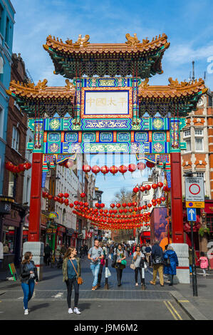 LONDON - MARCH 30, 2017: Tourists walk beneath an ornate gate marking the entrance to Chinatown, on Gerrard Street in Westminster. Stock Photo