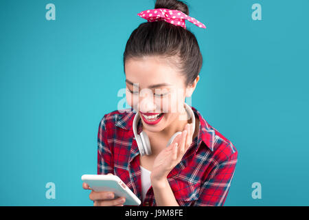 Happy young asian woman using smartphone standing over blue. Stock Photo