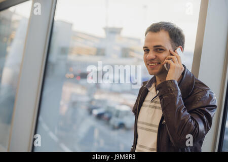 Young traveler on an airport, with a leather jacket talking on his smartphone Stock Photo