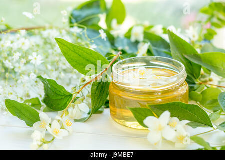 Honey in glass jars with jasmine flowers on windowsill. Shallow depth of field. Stock Photo