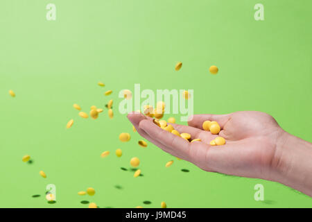 Flying yellow pills from hand in front of green background Stock Photo