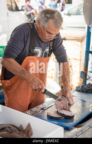 A fishmonger cutting up fish on a market stall in the market at Marsaxlokk Malta Stock Photo