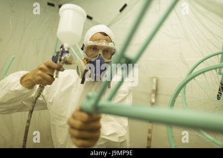 Painter painting bicycle frame through paint spray gun at workshop Stock Photo