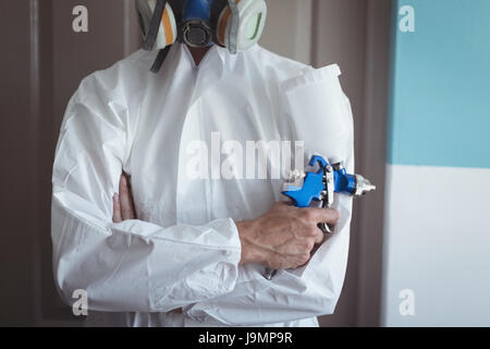Mid section of employee holding paint spray gun while wearing gas mask at bicycle workshop Stock Photo
