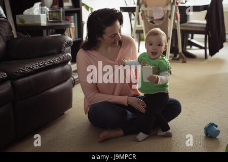 Smiling baby girl sitting on her mothers lap using mobile phone in living room Stock Photo