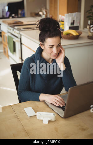 Woman sitting at kitchen table using laptop at home Stock Photo