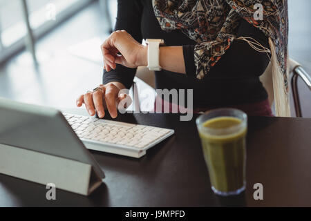 Female executive checking time on her watch while working on digital tablet in office cafeteria Stock Photo
