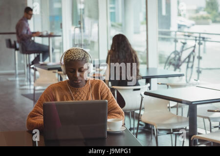 Female executive with headphones using laptop in office cafeteria Stock Photo