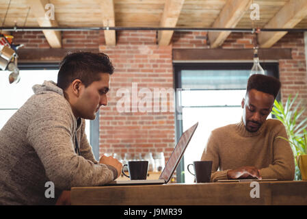 Gay couple using digital tablet and laptop while having coffee at home Stock Photo