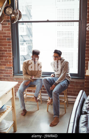 Gay couple using digital tablet while sitting on stool at home Stock Photo