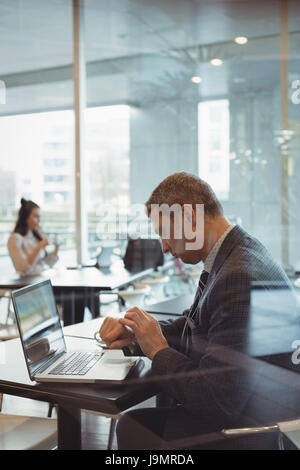 Businessman checking time while using laptop in office cafeteria Stock Photo