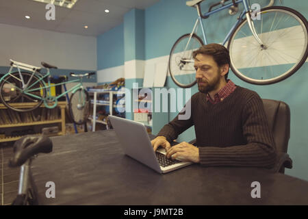 Focused employee using laptop on desk at bicycle workshop Stock Photo