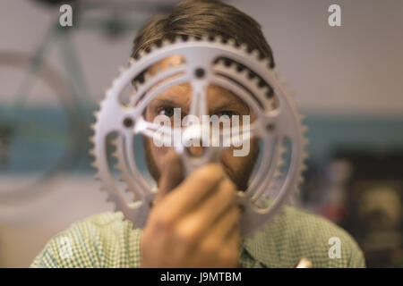 Portrait of employee looking through bicycle gear at repair shop Stock Photo