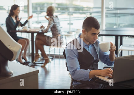 Businessman having coffee while using laptop in office cafeteria Stock Photo