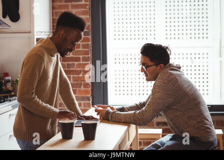 Gay couple using digital tablet and mobile phone in the kitchen at home Stock Photo