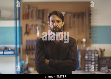 Portrait of serious owner standing with arms crossed at bicycle workshop Stock Photo