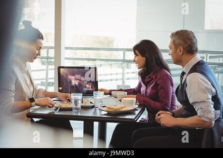 Businesspeople discussing over laptop in office cafeteria Stock Photo