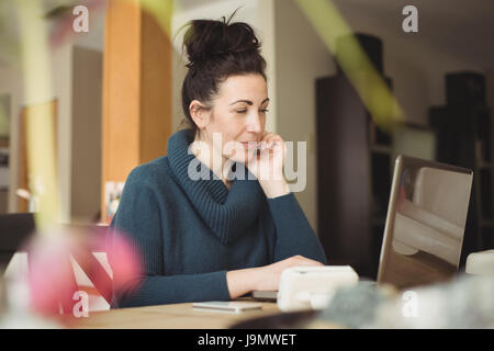 Woman sitting at kitchen table using laptop at home Stock Photo
