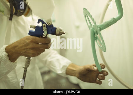 Painter painting bicycle gear through paint spray gun at workshop Stock Photo