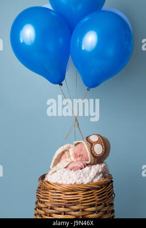 Sleeping nine day old newborn baby boy wearing an aviator hat and sleeping in a pretend hot air balloon. Stock Photo