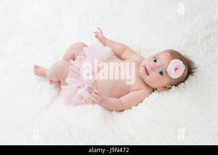 Portrait of a four month old baby girl wearing frilly, pink bloomers and a pink, flower headband. Shot in the studio on a white blanket. Stock Photo