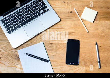 Work environment with a laptop, smartphone, notepad and other accessories on wooden table from above Stock Photo