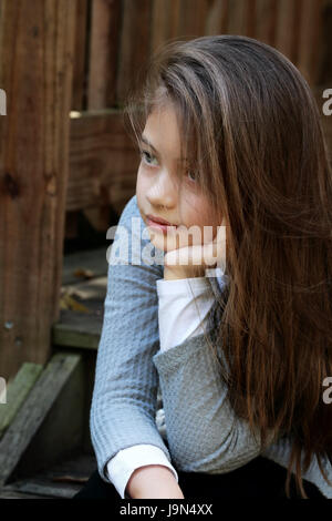 Young girl sitting on porch steps with long hair falling loosely around her face. Extreme shallow depth of field. Stock Photo