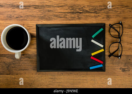 colored chalk is placed in a lightning shape on the blank blackboard of copyspace showing on wooden floor background with hot black coffee and fashion Stock Photo