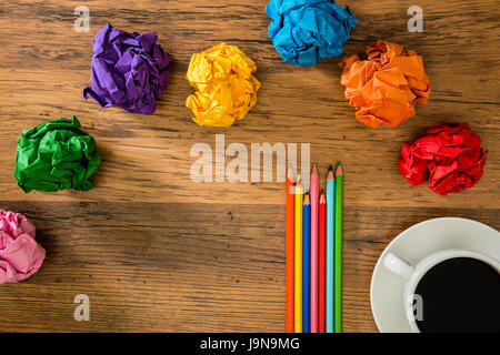 many rainbow colorful paper balls and color pencils on wooden desk background to showing advertising copyspace for text or drawing area with a cup of 