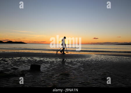metal detectorist at sunset on the beach looking for treasure Stock Photo