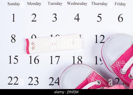 Pregnancy test with positive result and baby shoes lying on calendar, concept of extending family and expecting for baby Stock Photo