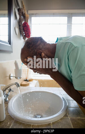 Side view of senior man washing his face at sink in bathroom Stock Photo