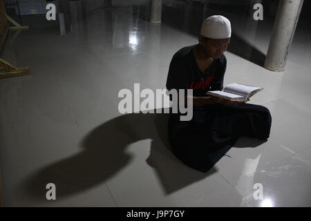 A young man reading Quran after following Taraweh prayer at the Jammi Annawawiyyah mosque during the holy month of Ramadhan, Muslims in Indonesia often their times in the mosque to perform various worship besides salat called I'tikaf, one of them by reading Quran. (Photo by Tubagus Aditya Irawan / Pacific Press) Stock Photo