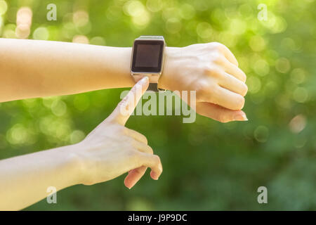 Close up shot of female forefinger pressing the button on blank screen smart watch outdoors. Modern technologies and apps concepts. Stock Photo