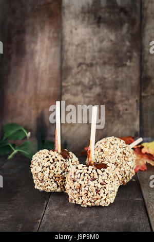 Three candy apples with nuts and caramel against a rustic wooden background. Shallow depth of field with selective focus on foreground. Stock Photo