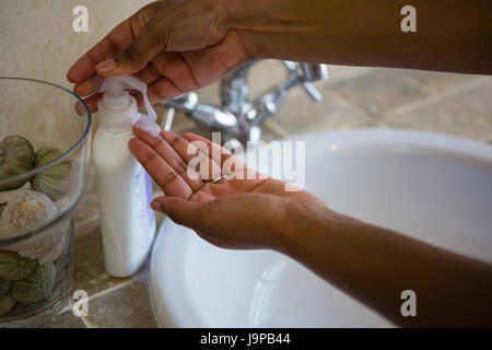 Cropped hands using soap dispenser by sink in bathroom at home Stock Photo