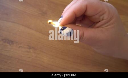 female hand holding a burning match over the table Stock Photo