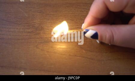 female hand holding a burning match over the table Stock Photo