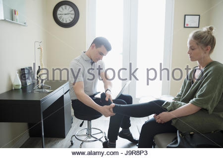 Male physiotherapist examining ankle of woman in clinic examination room