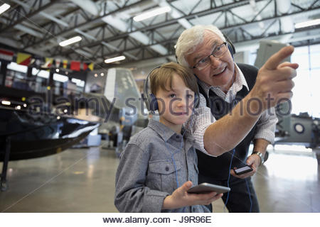 Grandfather and grandson with headphones looking at airplane exhibit in war museum hangar
