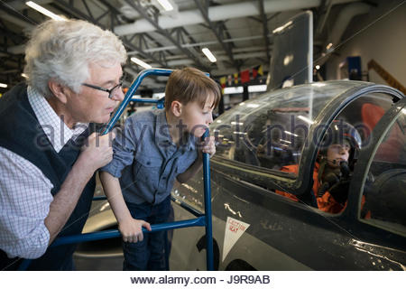 Grandfather and grandson looking into airplane cockpit in war museum hangar