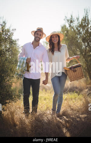 Portrait of happy young couple carrying picnic basket at olive farm Stock Photo
