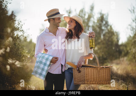 Happy young couple looking at each other while carrying picnic basket at olive farm Stock Photo