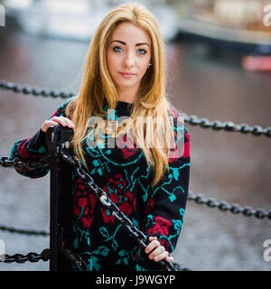 Alex gently holds onto the chains and railings which surround the water in the Albert Dock (Liverpool) as her long hair falls over her shoulders. Stock Photo