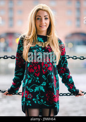 A three quarter length portrait as she leans back on the chain railings which surround the water in the Albert Dock, Liverpool. Stock Photo