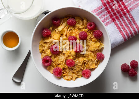 Breakfast cereal of cornflakes and raspberries, honey and milk on white table Stock Photo