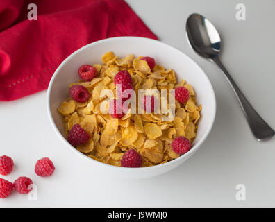 Cornflakes breakfast cereal with raspberries in bowl on white table with selective focus Stock Photo